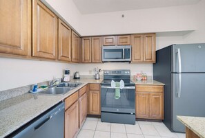 A kitchen with wooden cabinets, a stainless steel microwave, a black oven, and a refrigerator. - 2B Resort Condo w/ Pool View 7 minutes to Disney (Orlando)
