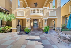 A courtyard with a checkered floor, potted plants, outdoor seating, and a central balcony. - Floridays 505D: 2BR for 6, Heated Pools, Free Parking & No Resort Fees (Orlando)