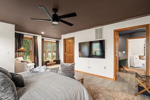 Ein modernes Schlafzimmer mit einem großen Bett, einem Deckenventilator, einem Fernseher und Blick ins Freie durch die Fenster.