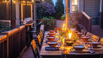 An outdoor dining area with a long wooden table set for a meal, surrounded by chairs.