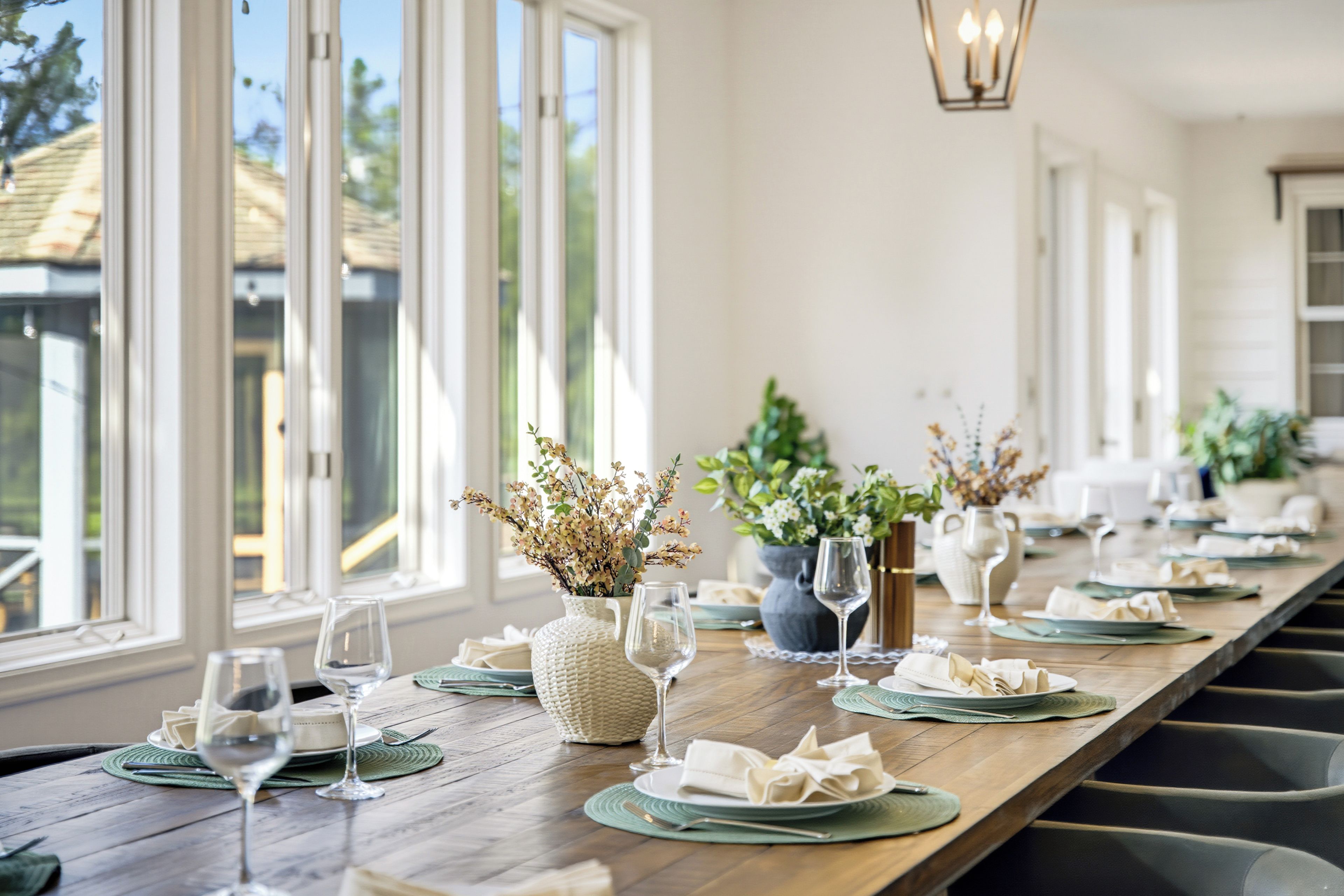 Une longue table à manger, dressée avec soin et comprenant de nombreuses pièces, notamment des assiettes, des verres et des vases décoratifs.