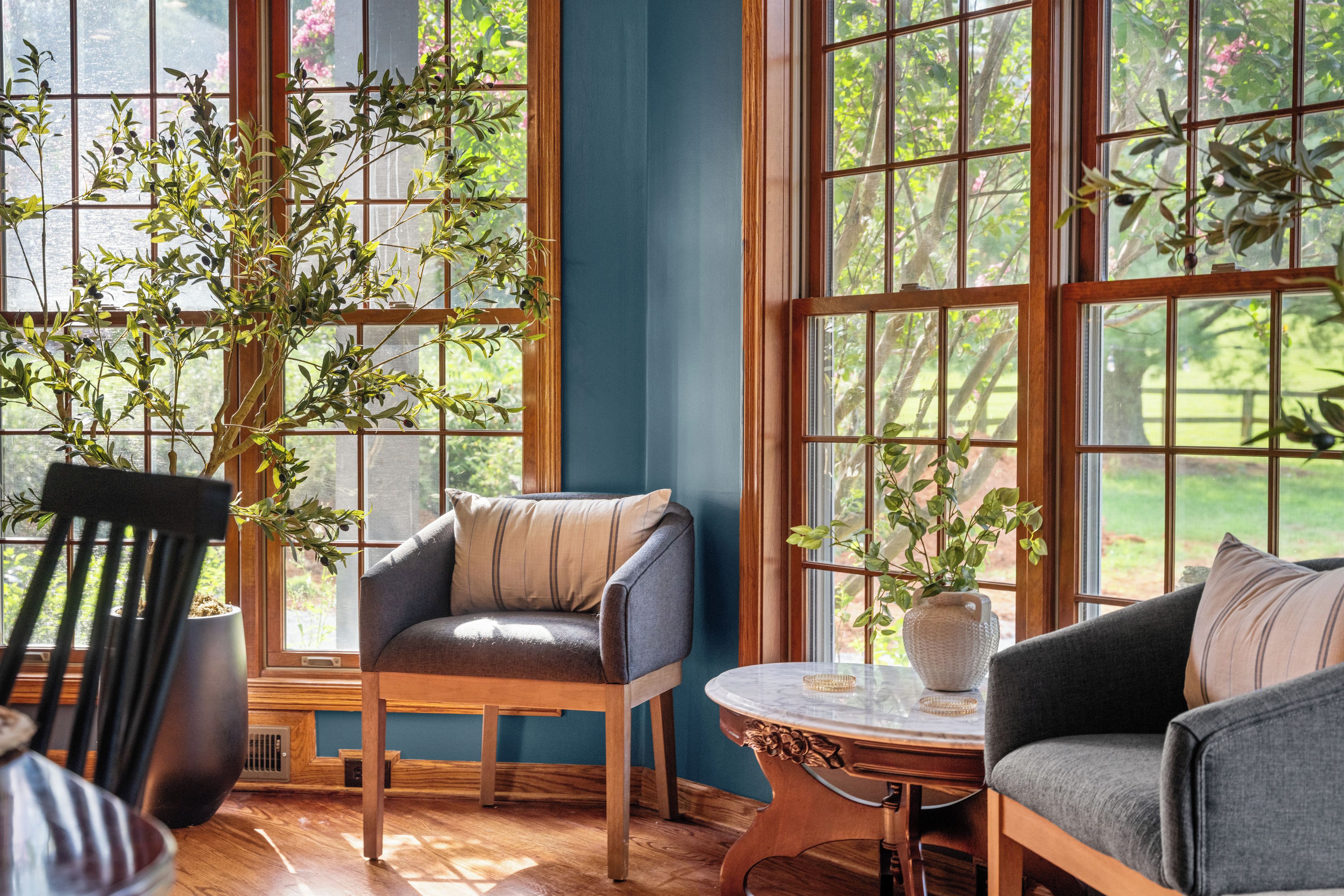 A room with large windows, a wooden chair, a sofa, and a small table.