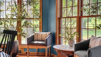 A room with large windows, a wooden chair, a sofa, and a small table.