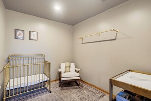 Ein Babyzimmer mit einem Babybett, einer Wickelkommode, einem Stuhl und einem kleinen Tisch.