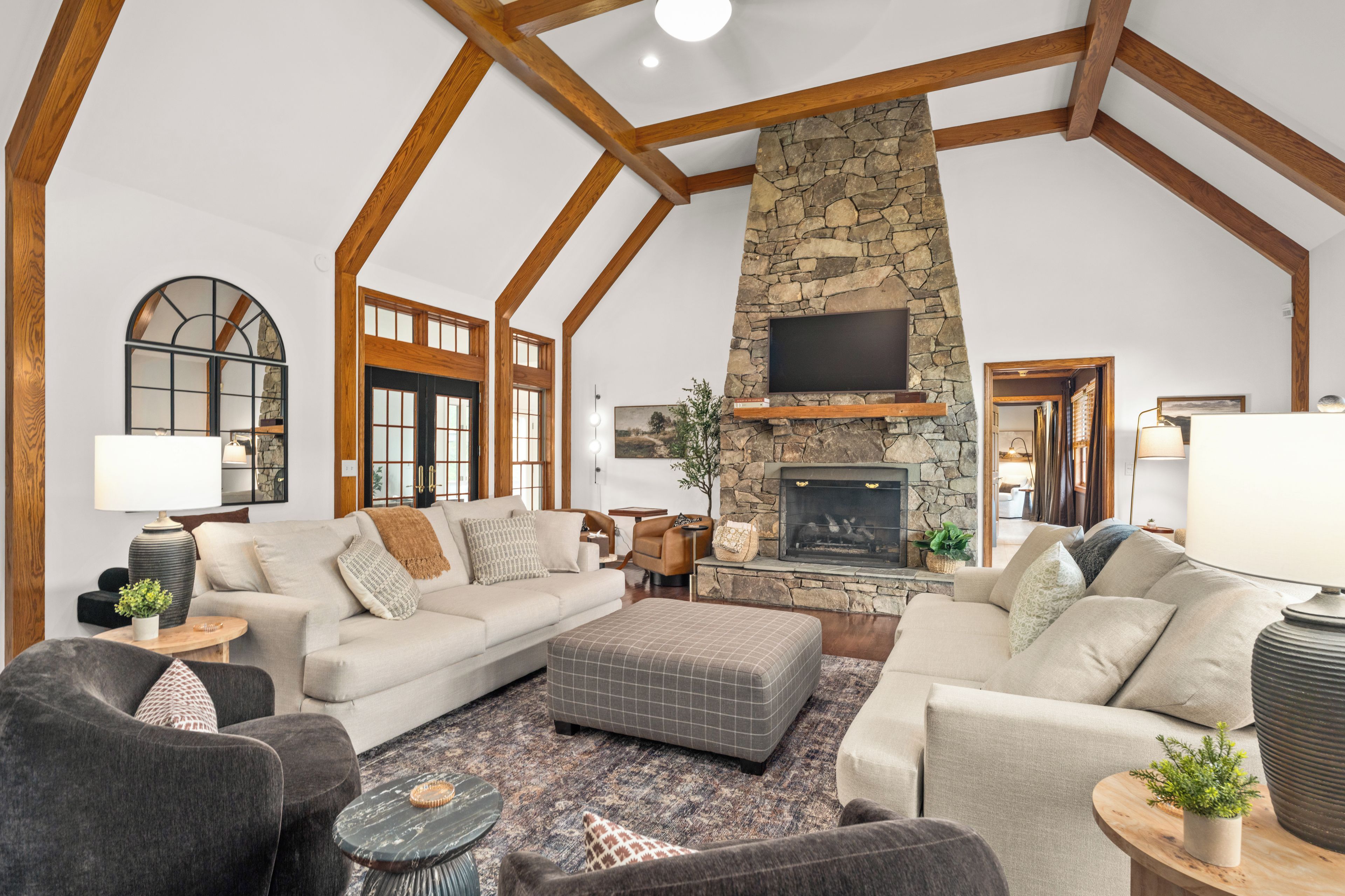 A spacious living room with a stone fireplace, wooden beams, and a large window.