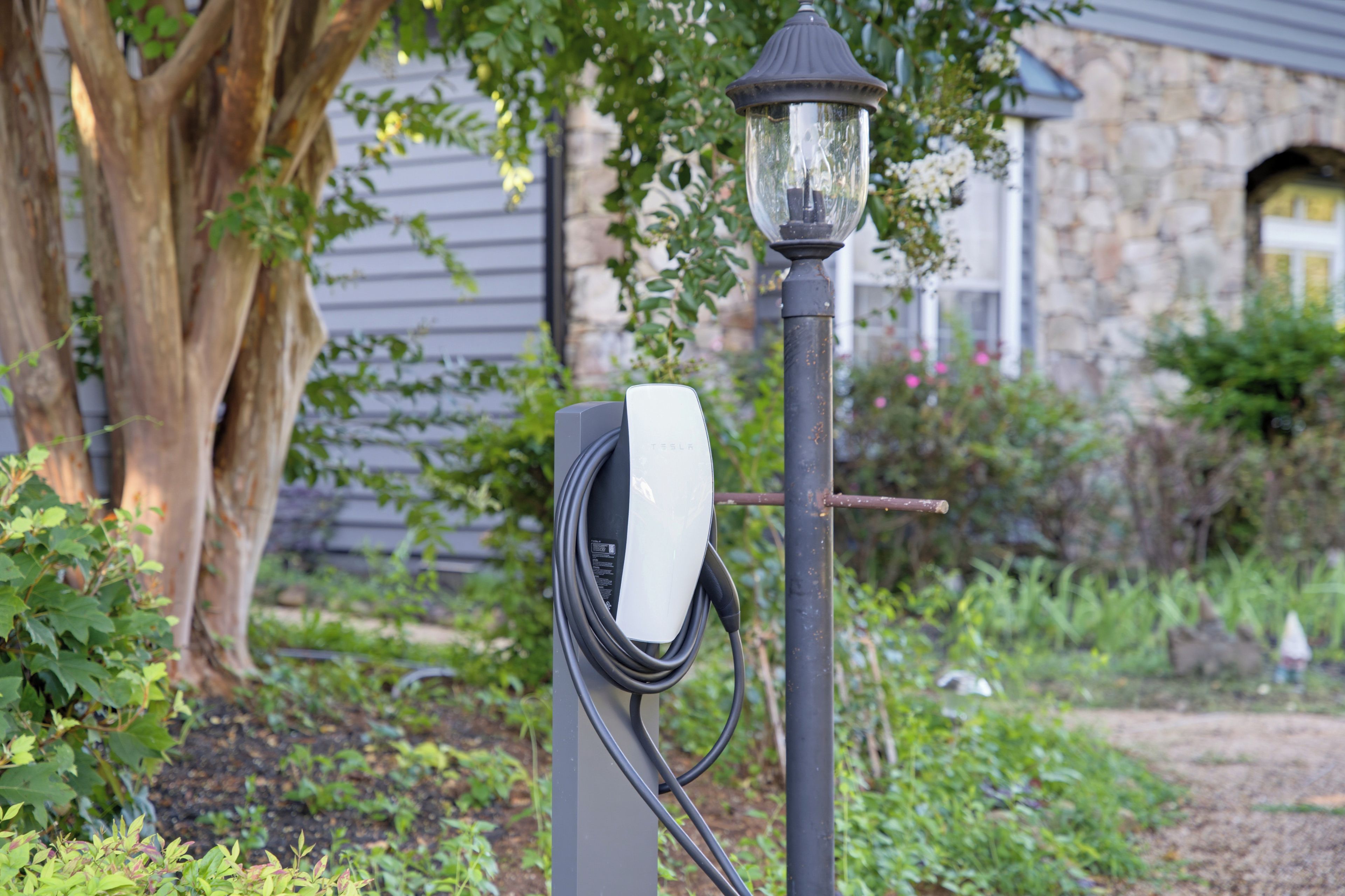 Eine Ladestation mit Kabel und einer Laterne in einem Garten.