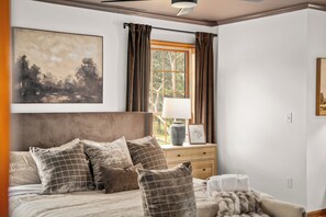 Ein Schlafzimmer mit einem großen Bett, einem Nachttisch, einem Fenster mit Vorhängen und einem Bild an der Wand.