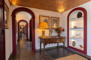 A hallway with a wooden table, a lamp, and a vase with flowers. There are framed pictures on the wall and a shelf with decorative items. - 196 Monte da Palhavã (Montemor-o-Novo)