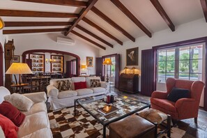 A spacious living room with a high ceiling, a checkered floor, and a view of the outdoors through large windows.