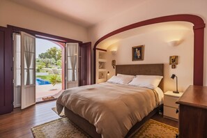 A bedroom with a bed, a nightstand, a lamp, and a view of a swimming pool. - 196 Monte da Palhavã (Montemor-o-Novo)