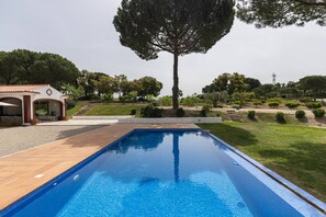 A swimming pool with a tiled deck, surrounded by a landscaped garden with various trees and shrubs.