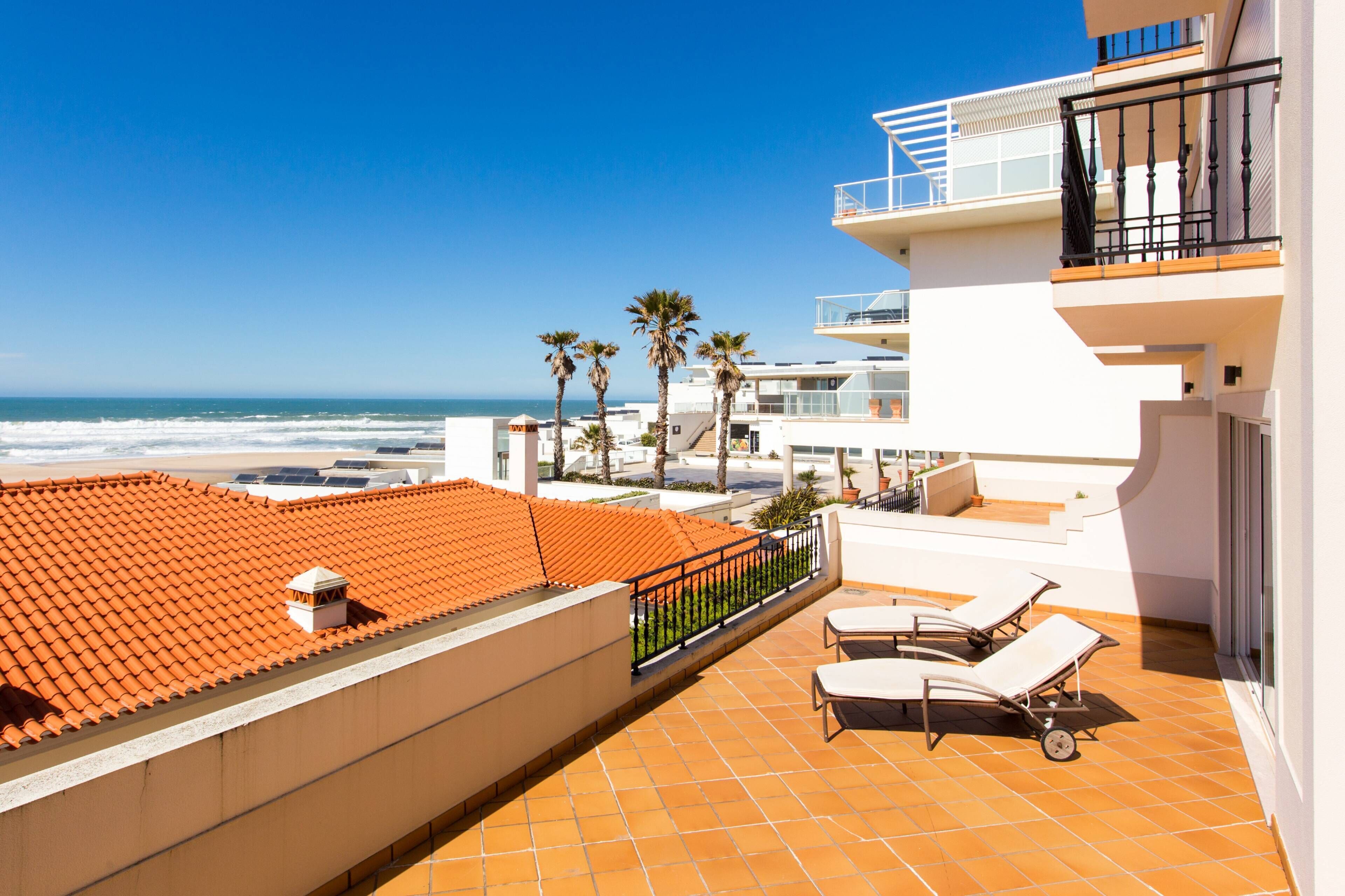 A rooftop terrace with a view of the ocean, a pool, and a lounge area.