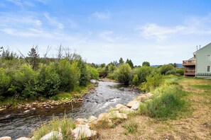 A river flowing through a natural landscape with a wooden bridge and a house on the right.
