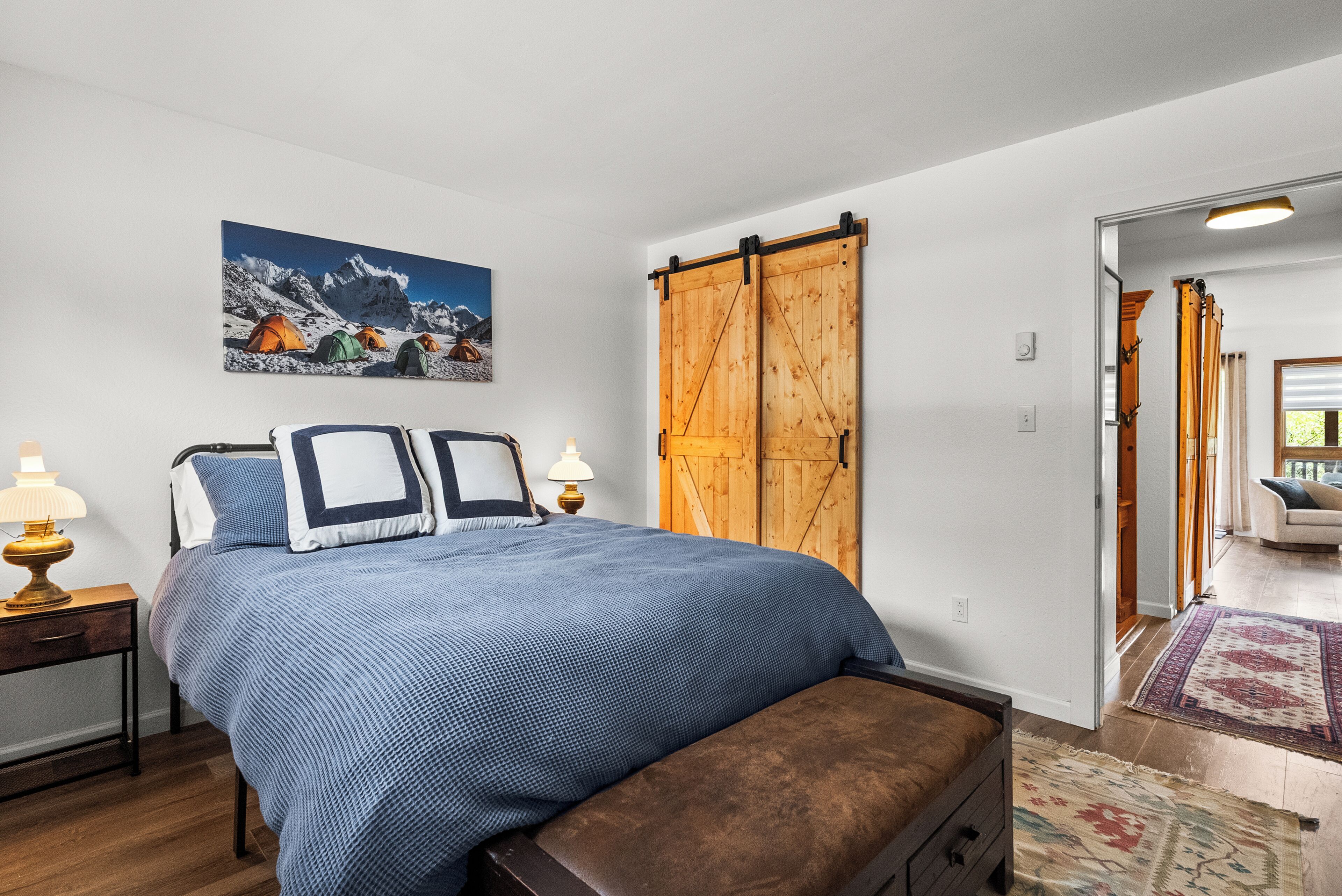 Une chambre à coucher avec un grand lit, une porte coulissante en bois, un tableau représentant des montagnes et une lampe sur une table de chevet.