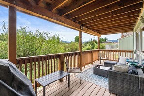 A covered outdoor deck with a wooden railing, a table, a chair, and a sofa.