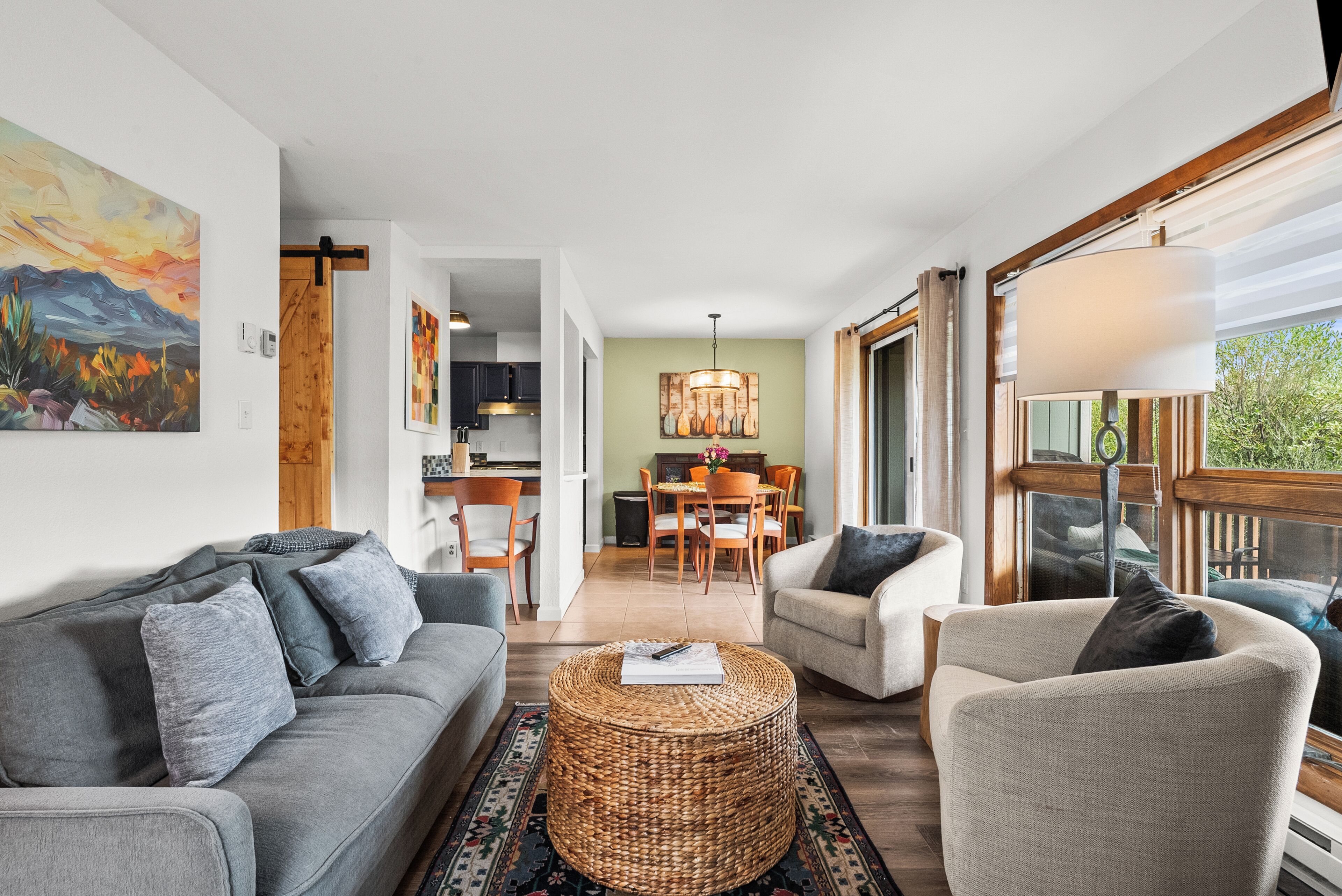 Un salon moderne avec un canapé gris, une table basse en osier et un coin repas comprenant des chaises et une table en bois.