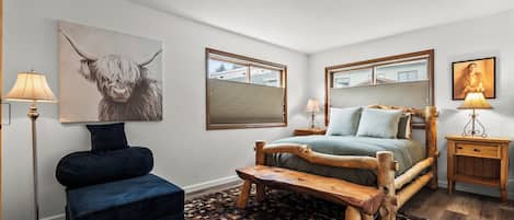 A bedroom with a bed, a bench, a chair, a lamp, and a painting on the wall.