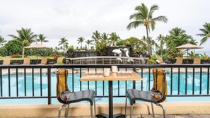 A poolside area with two chairs and a table, overlooking a pool with a dolphin sculpture. - Big Island Resort Stay Near Kona Coast with Pools & Spacious 1BR Villa (Kailua-Kona)