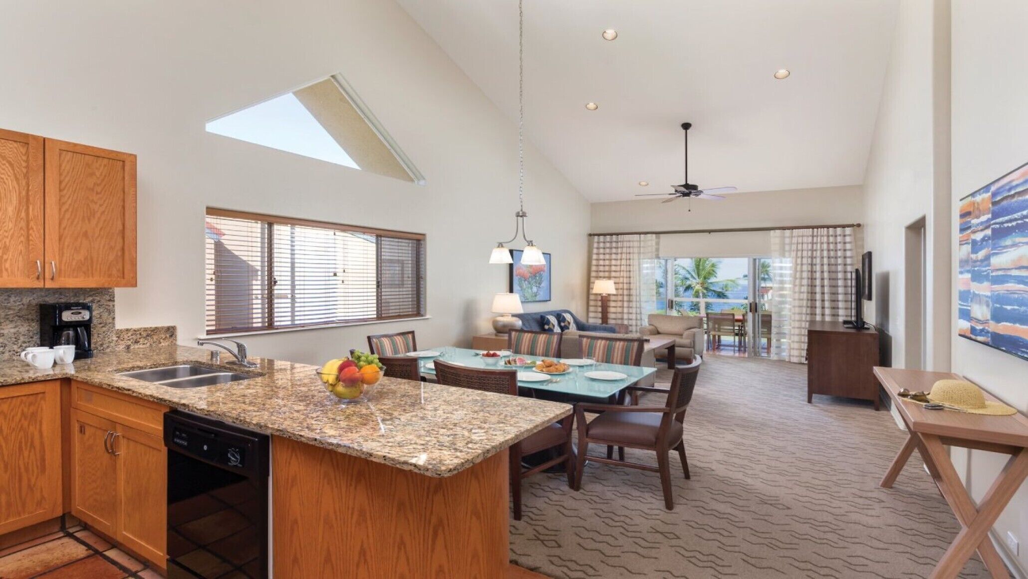A spacious kitchen with granite countertops, wooden cabinets, and a dining area with a high ceiling and ceiling fan.