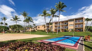 A hotel with a pool area, palm trees, and a tennis court.