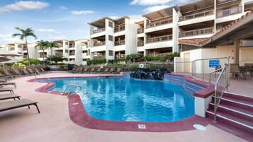 A swimming pool with a waterfall feature, surrounded by lounge chairs and a multi-story building with balconies.