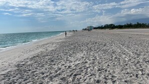 A beach with a wide sandy area, a few buildings in the distance, and a clear sky. - Charming Manasota Key Beach Retreat, steps to the beach, sleeps 6 (Englewood)