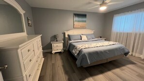 A bedroom with a bed, nightstands, a dresser, a ceiling fan, and a window with curtains. - Charming Manasota Key Beach Retreat, steps to the beach, sleeps 6 (Englewood)
