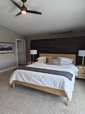 Ein Schlafzimmer mit einem Bett, zwei Nachttischlampen, einem Deckenventilator, einem dunklen Holz-Kopfteil, einer Tür und einem an der Wand hängenden Bild.