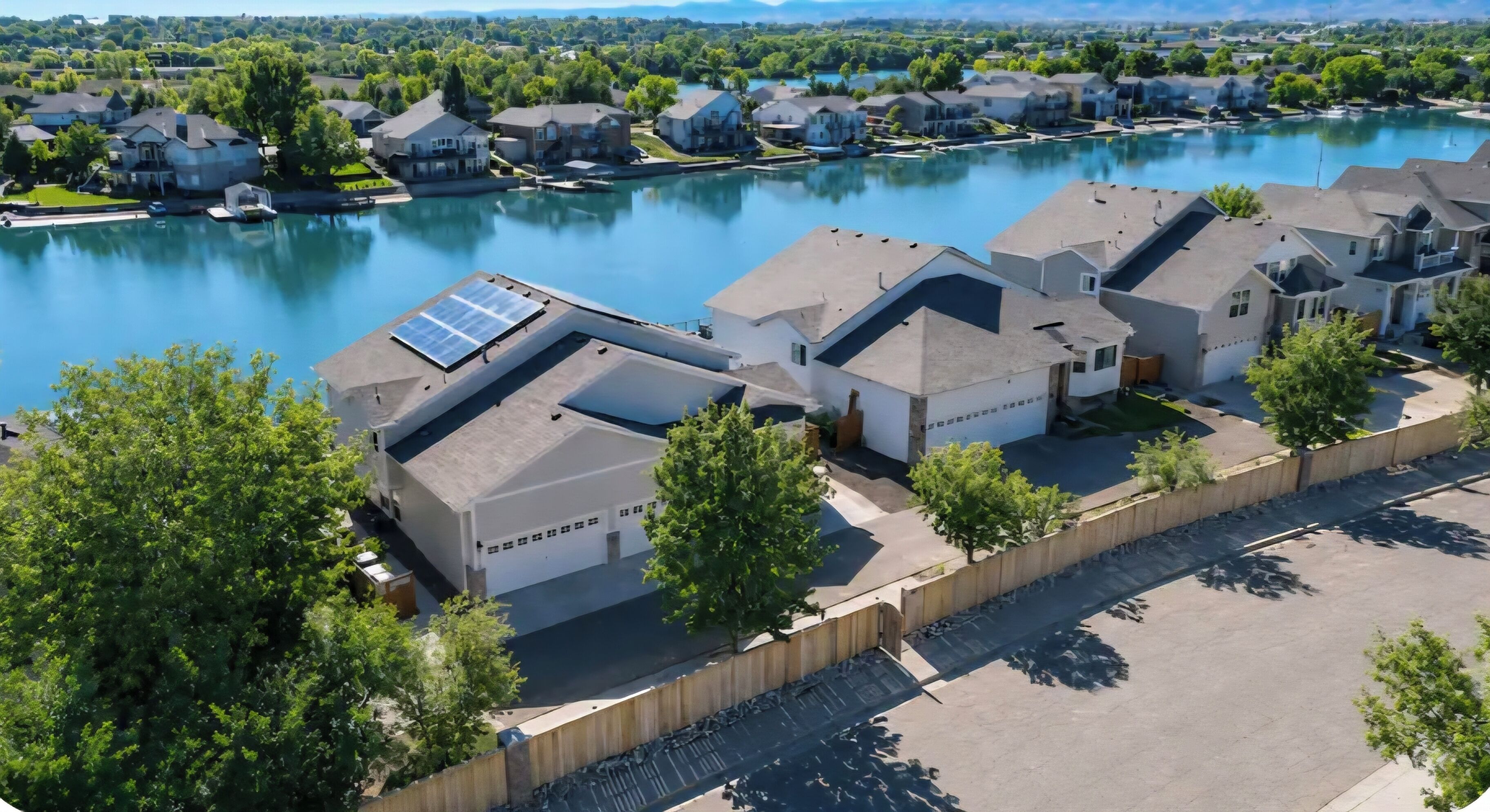 A residential area with houses, a body of water, and solar panels on rooftops.