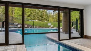 A swimming pool with a view of a forested area through large glass doors.