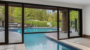 A swimming pool with a view of a forested area through large glass doors. - 2BR Suite at WorldMark Canmore-Banff Near Banff National Park & Skiing (Canmore)