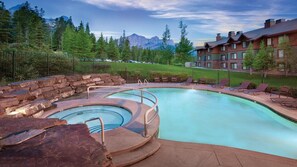 A pool with a hot tub, lounge chairs, and a view of mountains.