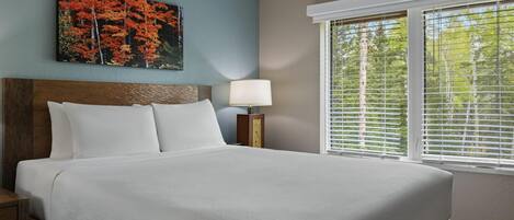 Una habitación de hotel con una cama, una mesita de noche, una lámpara, una ventana con persianas y un cuadro en la pared.