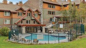 A residential building with a pool, outdoor seating, and a stone facade.