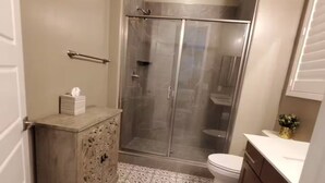 Ein Badezimmer mit Dusche, Toilette, Waschtisch und Fliesenboden mit Muster.