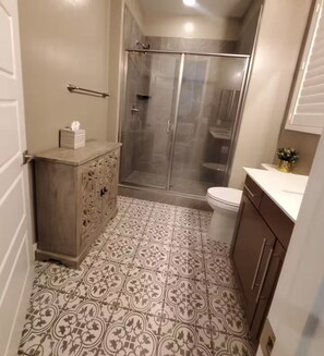 Een badkamer met douche, toilet, wastafel en vloertegels met patroon.