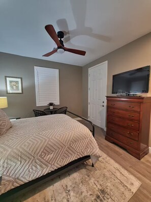 Een slaapkamer met een bed, een dressoir, een plafondventilator en een televisie.