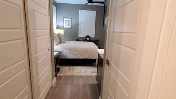 A hallway leading to a bedroom with a bed, a ceiling fan, and a window with blinds.