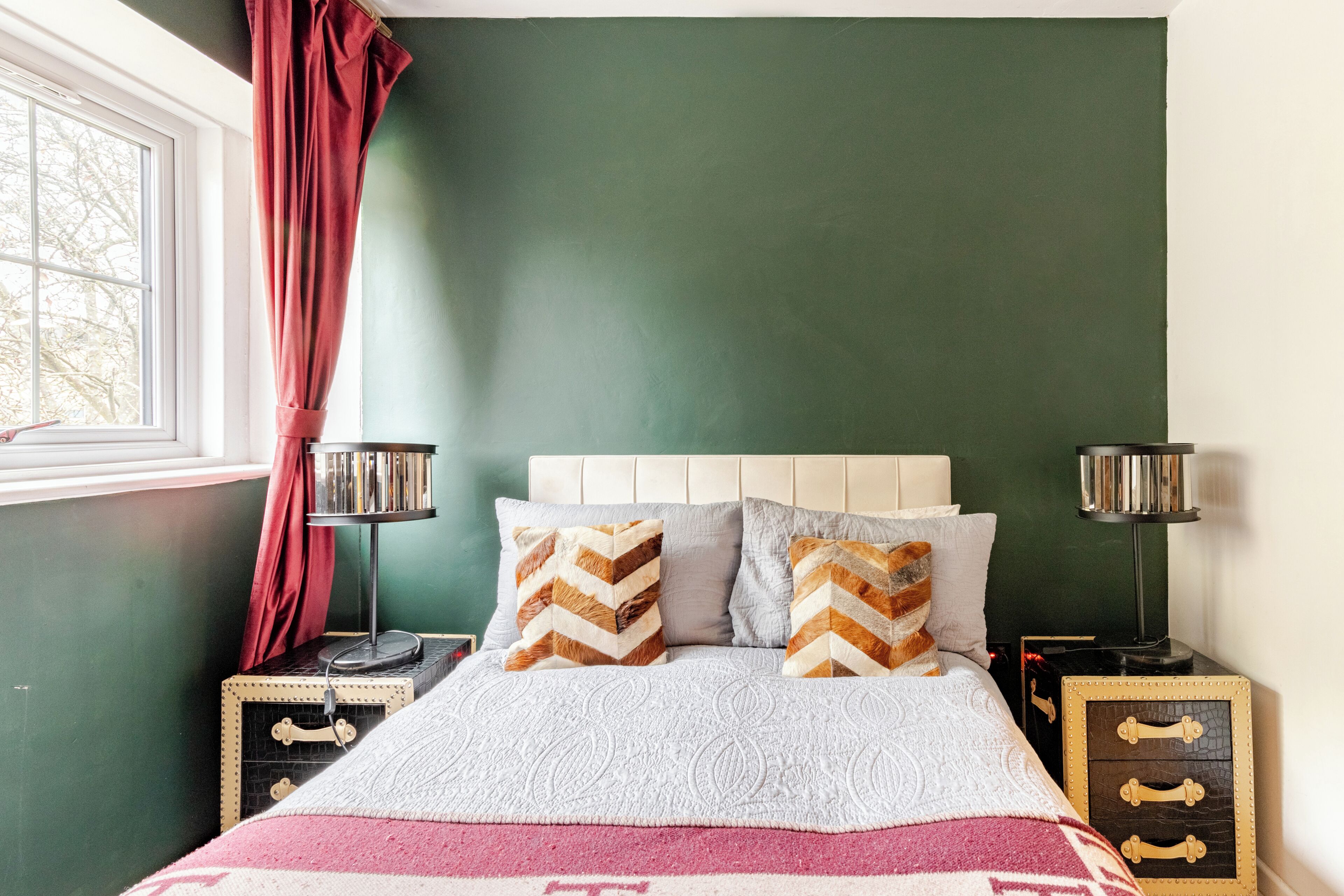 A bedroom with a bed, two bedside tables, a window with curtains, and a green wall.