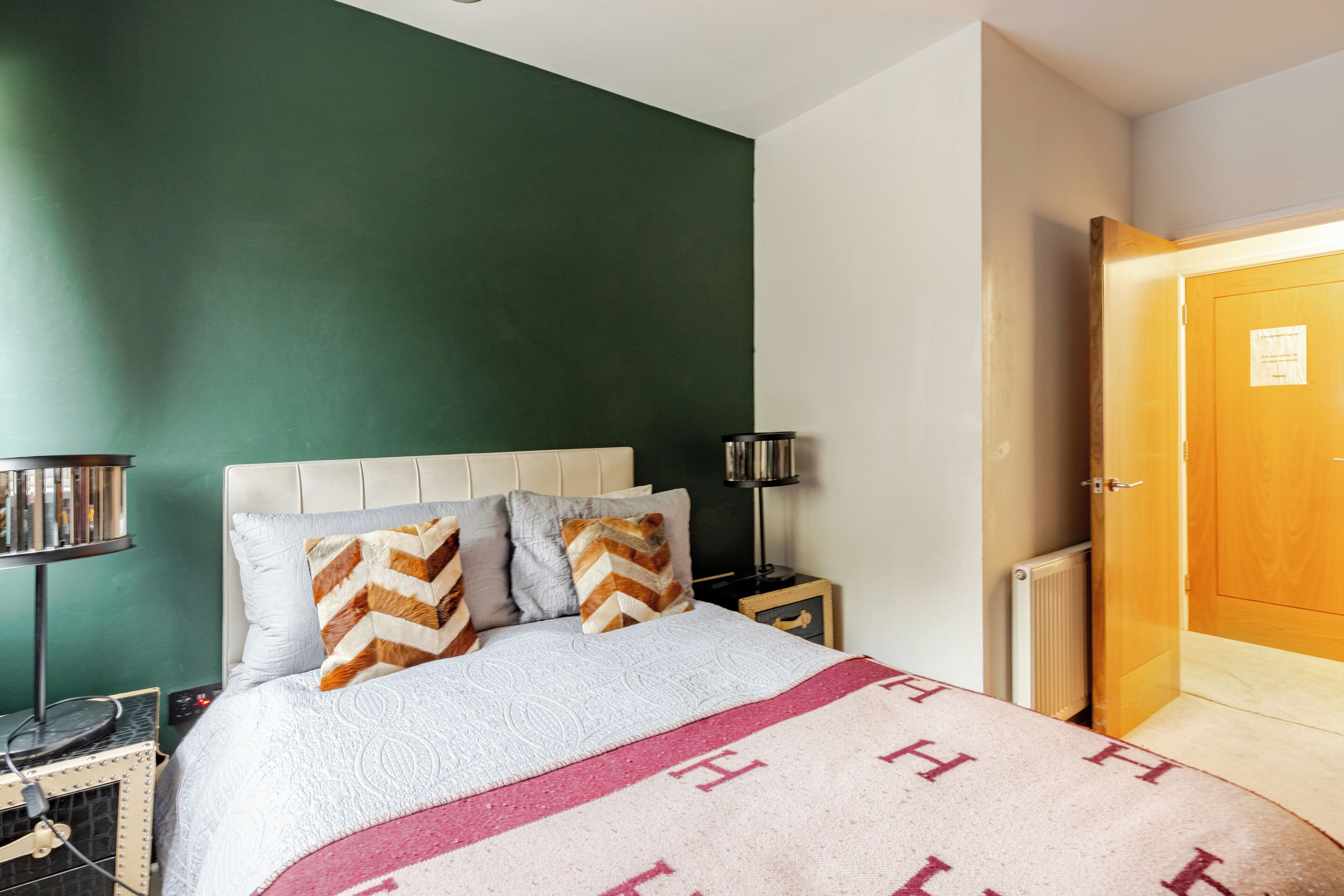 A bedroom with a bed, a nightstand, a lamp, and a door.