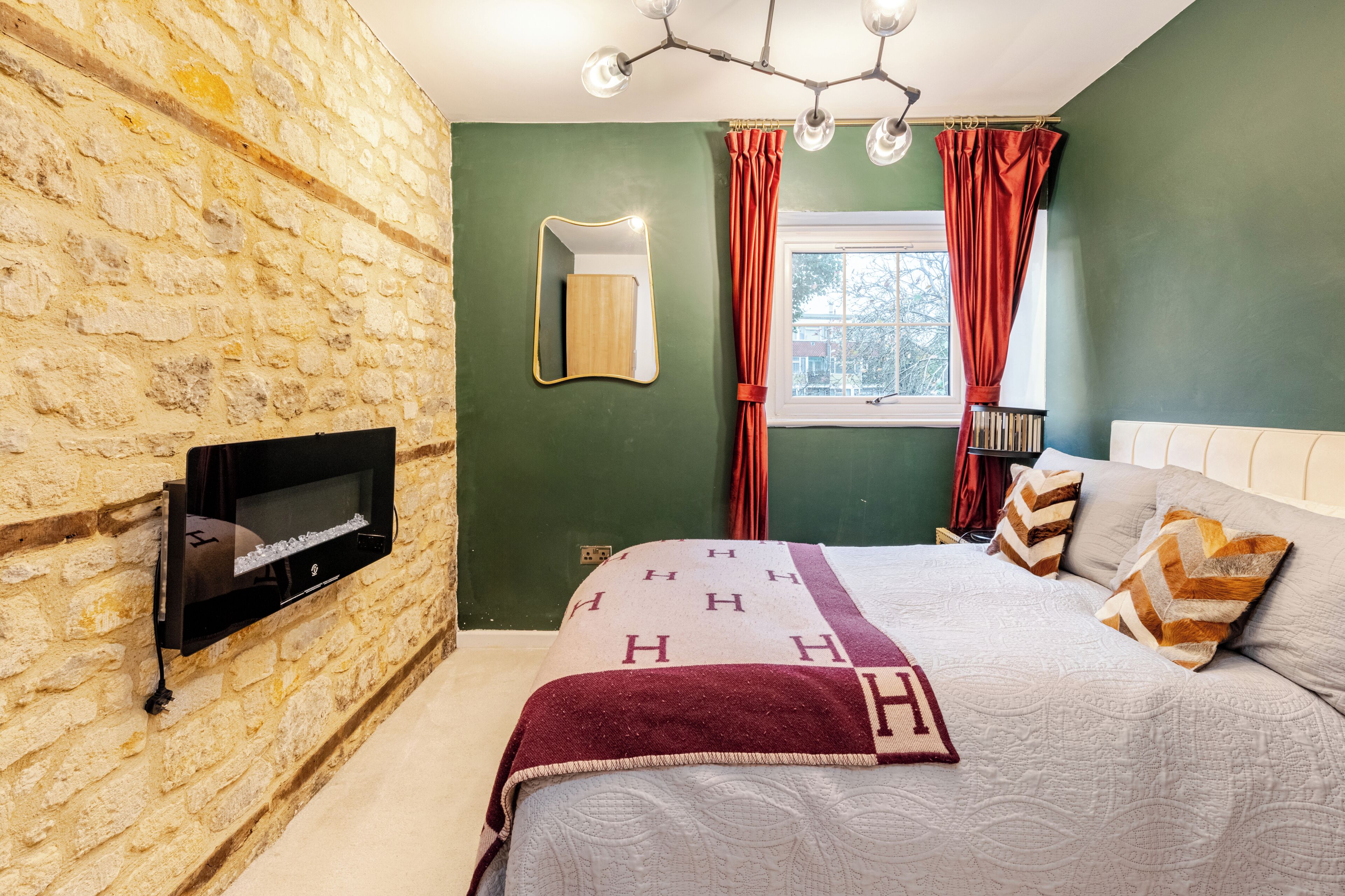 Ein Schlafzimmer mit Steinwand, einem Bett mit gemusterten Betttextilien, einem Wand-Fernseher und einem Fenster mit Vorhängen.