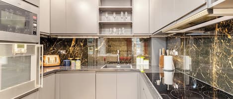 A modern kitchen with built-in appliances, a marble backsplash, and a stainless steel sink.