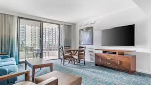 Une chambre d’hôtel avec un balcon, une télévision, une table à manger avec des chaises et un canapé.