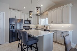 Una cocina moderna con una isla central, electrodomésticos de acero inoxidable e iluminación colgante.