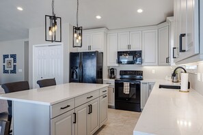 A modern kitchen with white cabinetry, a black refrigerator, a stainless steel stove, and pendant lighting. - Ogden Adventure Hub-Hike, bike, ski! Sleeps 7, 5 bedrooms, 3.5 bath home. (South Ogden)