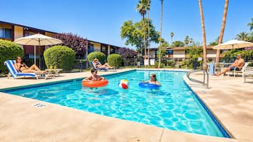 A swimming pool with lounge chairs and umbrellas, surrounded by palm trees and a building.
