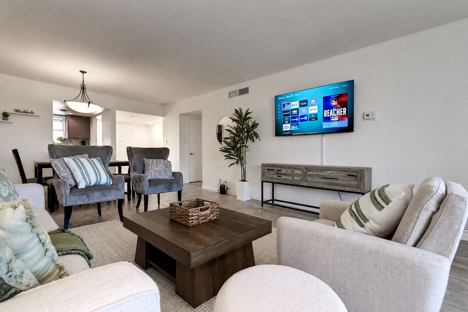 A modern living room with a flat-screen TV, two sofas, a coffee table, and a dining area in the background.