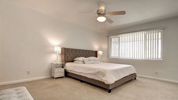 A bedroom with a bed, bedside tables, a ceiling fan, and a window with blinds.