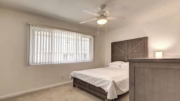 A bedroom with a bed, a ceiling fan, a window with blinds, and a wooden headboard.
