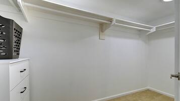 A room with white walls, a beige carpet, a white dresser with drawers, and a door with a silver handle.